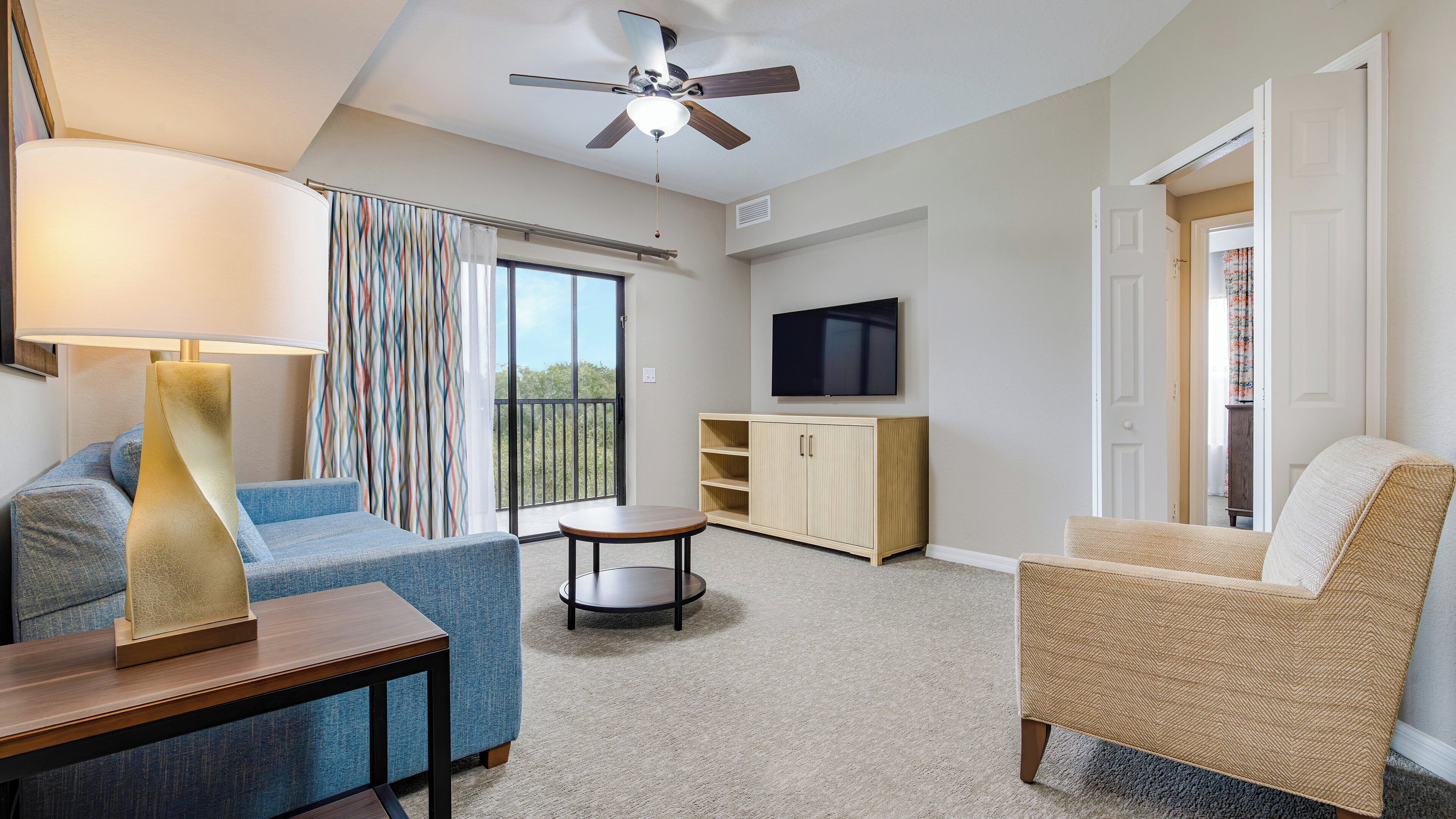 A living room with a sofa, armchair, TV, and a ceiling fan.
