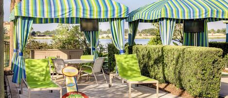 An outdoor seating area with striped umbrellas, a table, chairs, and a sign indicating a cabana rental.
