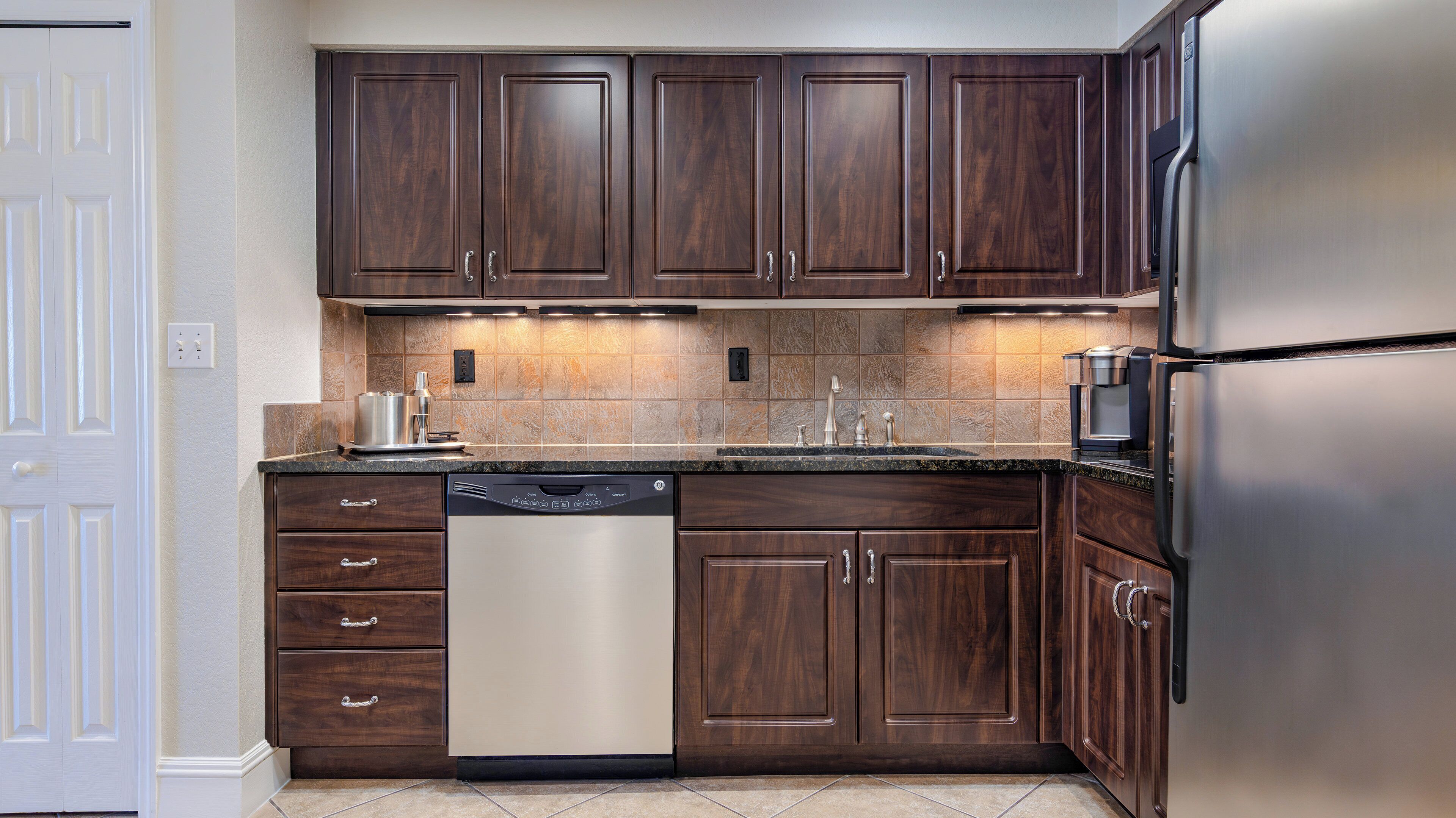 A kitchen with dark wooden cabinets, a stainless steel refrigerator, and a dishwasher.