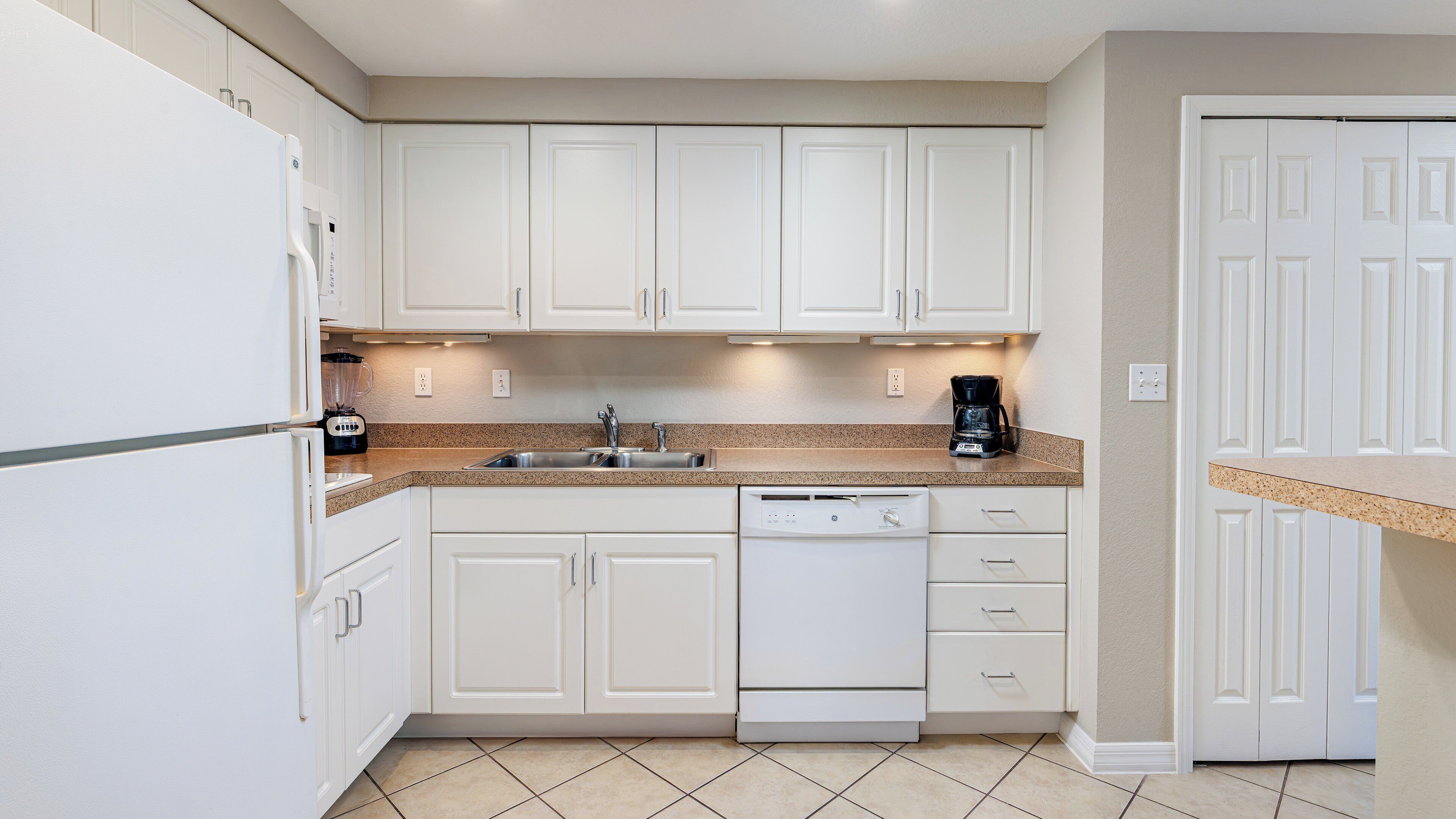 A kitchen with white cabinets, a granite countertop, a dishwasher, and a coffee maker.