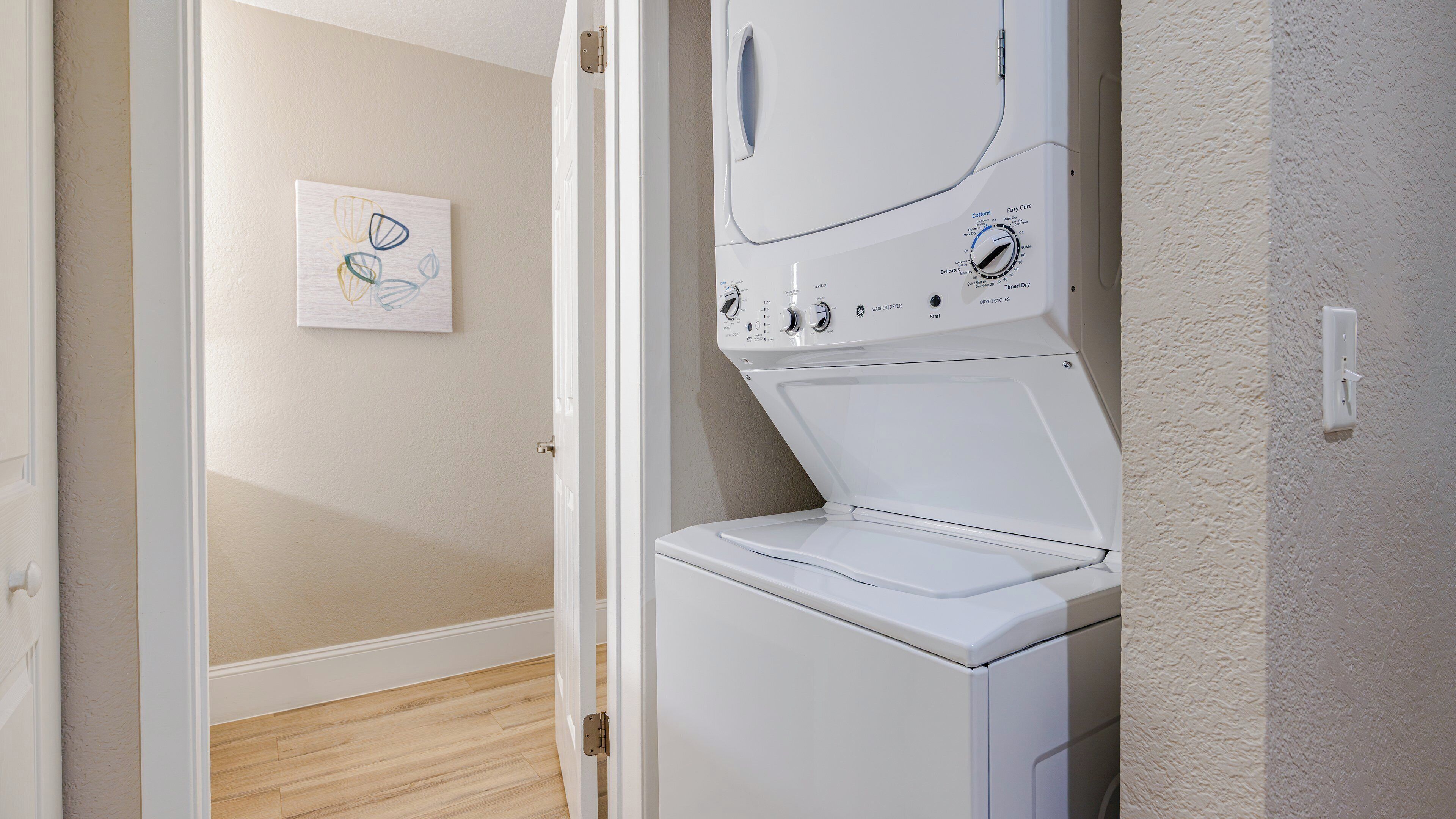 A laundry room with a front-loading washing machine, a door, and a wall-mounted light switch.