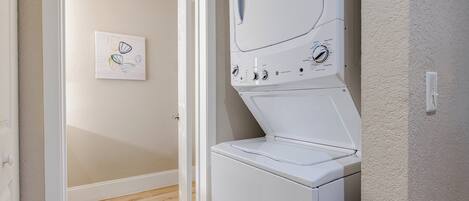 A laundry room with a front-loading washing machine, a door, and a wall-mounted light switch.