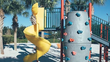 A playground with a yellow spiral slide and climbing wall with blue and orange grips.