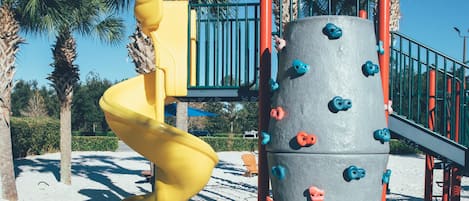 A playground with a yellow spiral slide and climbing wall with blue and orange grips.