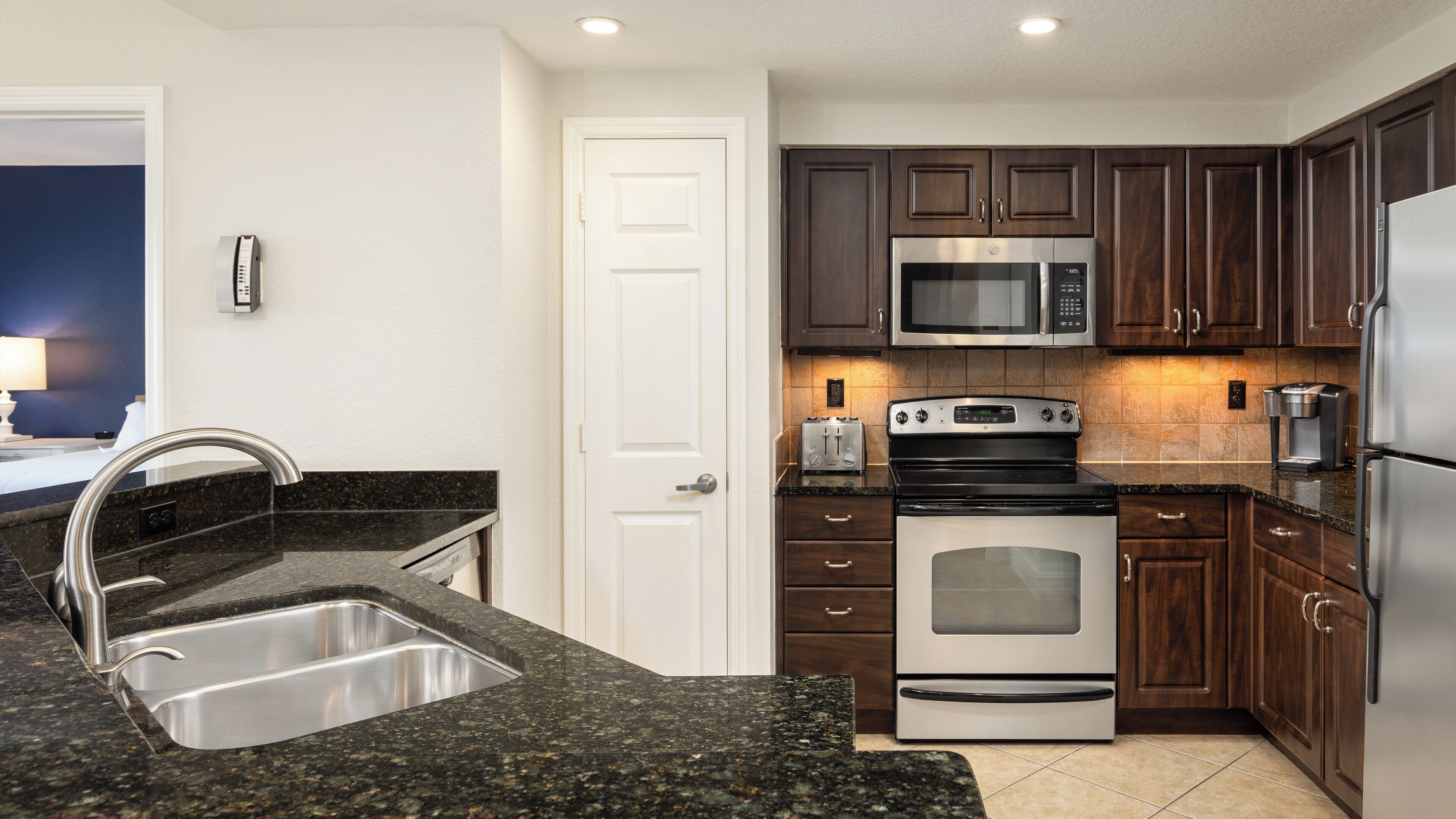 A modern kitchen with granite countertops, stainless steel appliances, and dark wood cabinetry.