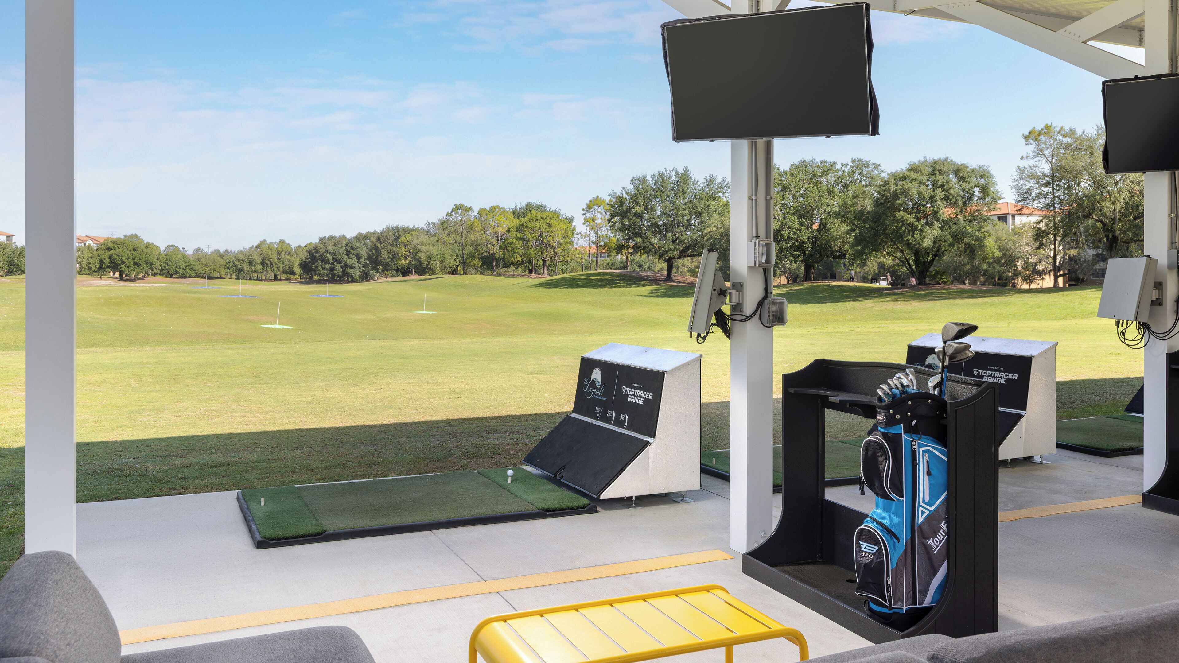 Un campo de prácticas de golf con vista despejada del campo, un bolso de golf y una pantalla de televisión.