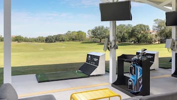 Un campo de prácticas de golf con vista despejada del campo, un bolso de golf y una pantalla de televisión.