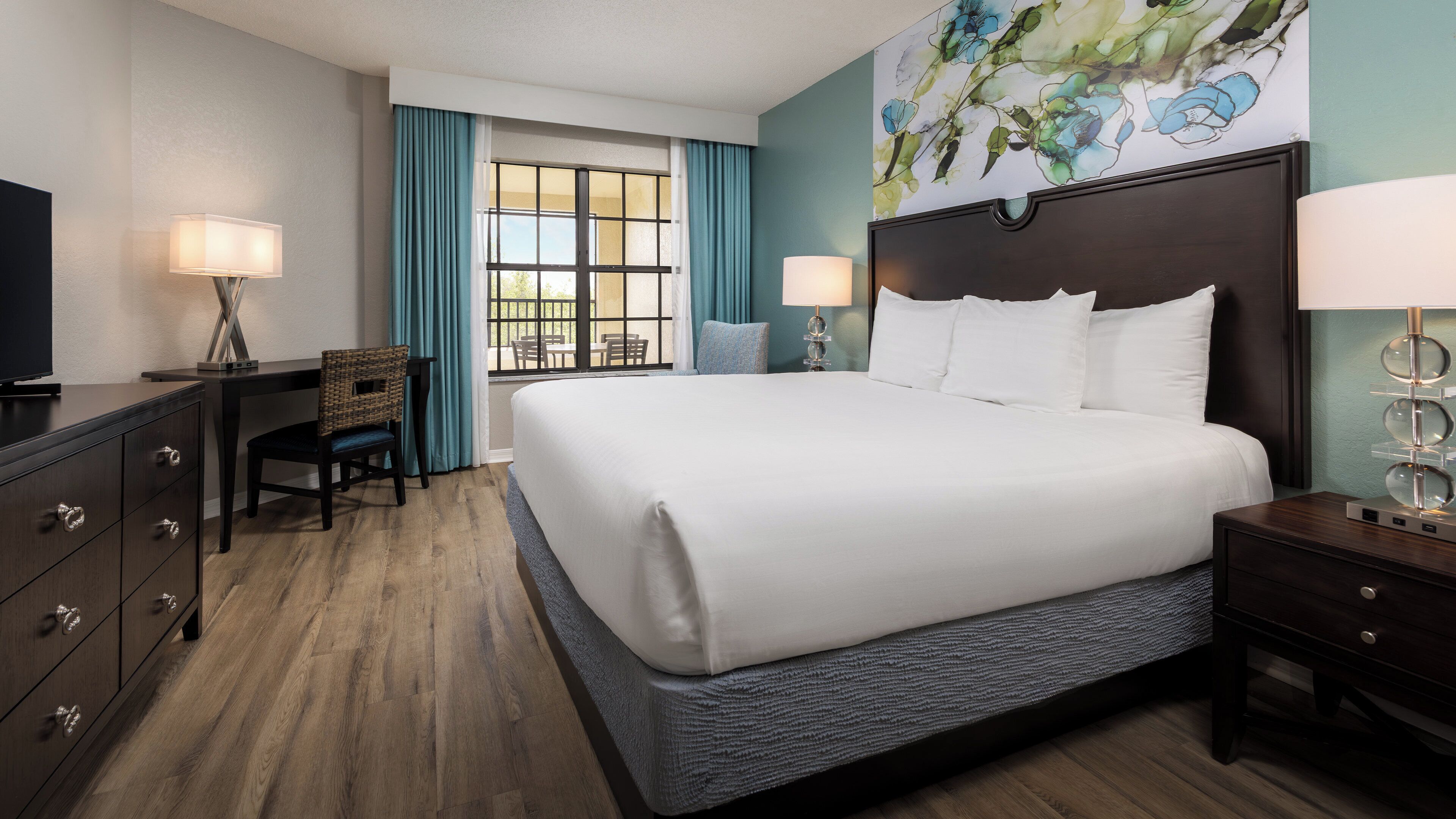 Een hotelkamer met een groot bed, een bureau, een stoel, een televisie en een schilderij aan de muur.
