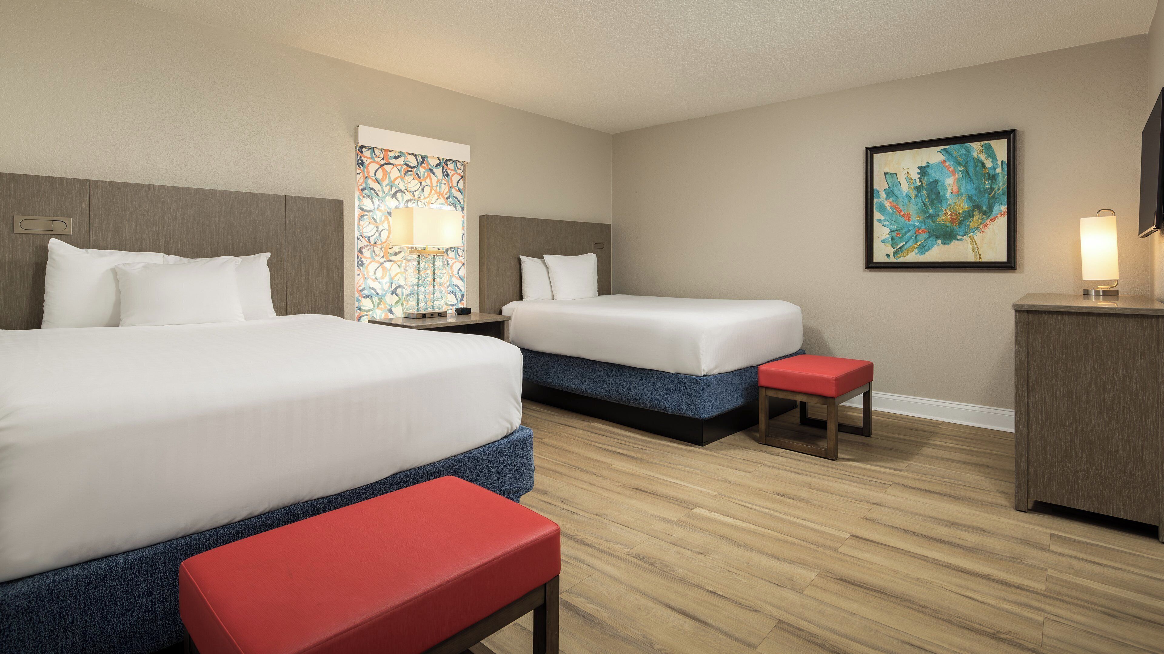 Habitación de hotel con dos camas, un escritorio, una silla y obras de arte en las paredes.