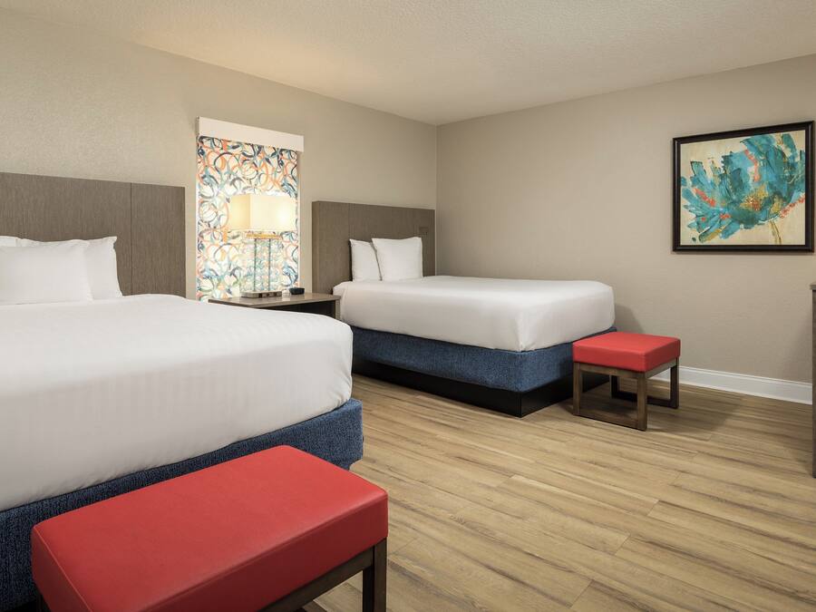 A hotel room with two beds, a desk, a chair, and artwork on the walls.