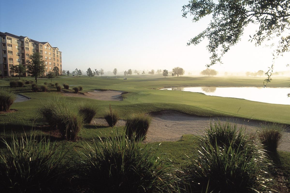 A golf course with bunkers, a pond, and a building in the background.