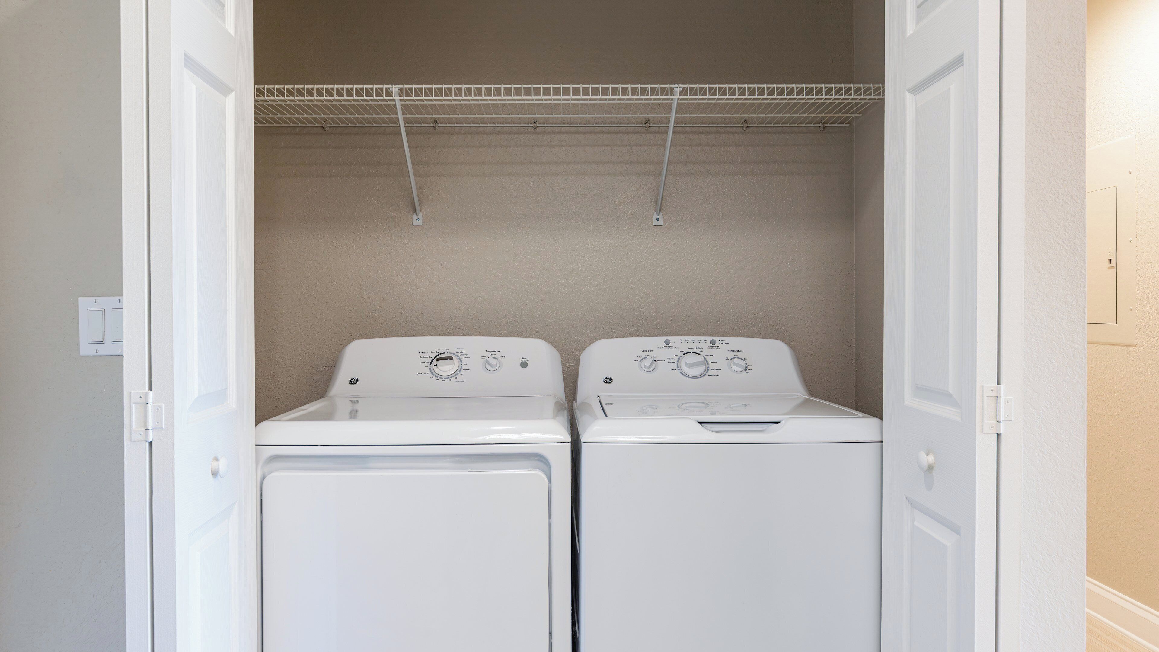 A laundry room with two front-loading washing machines and a metal drying rack above.