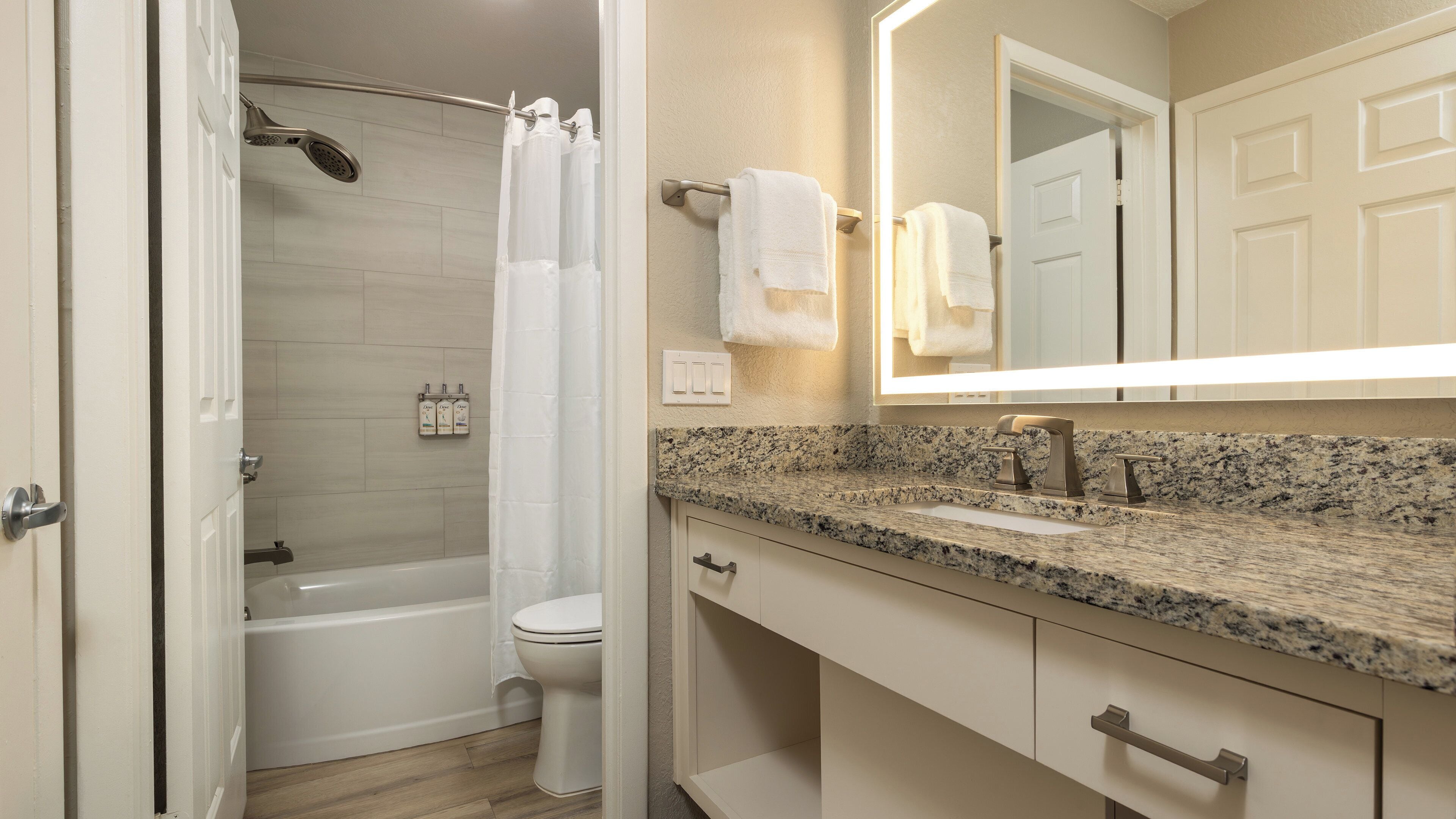 A bathroom with a shower, toilet, sink, and a mirror.