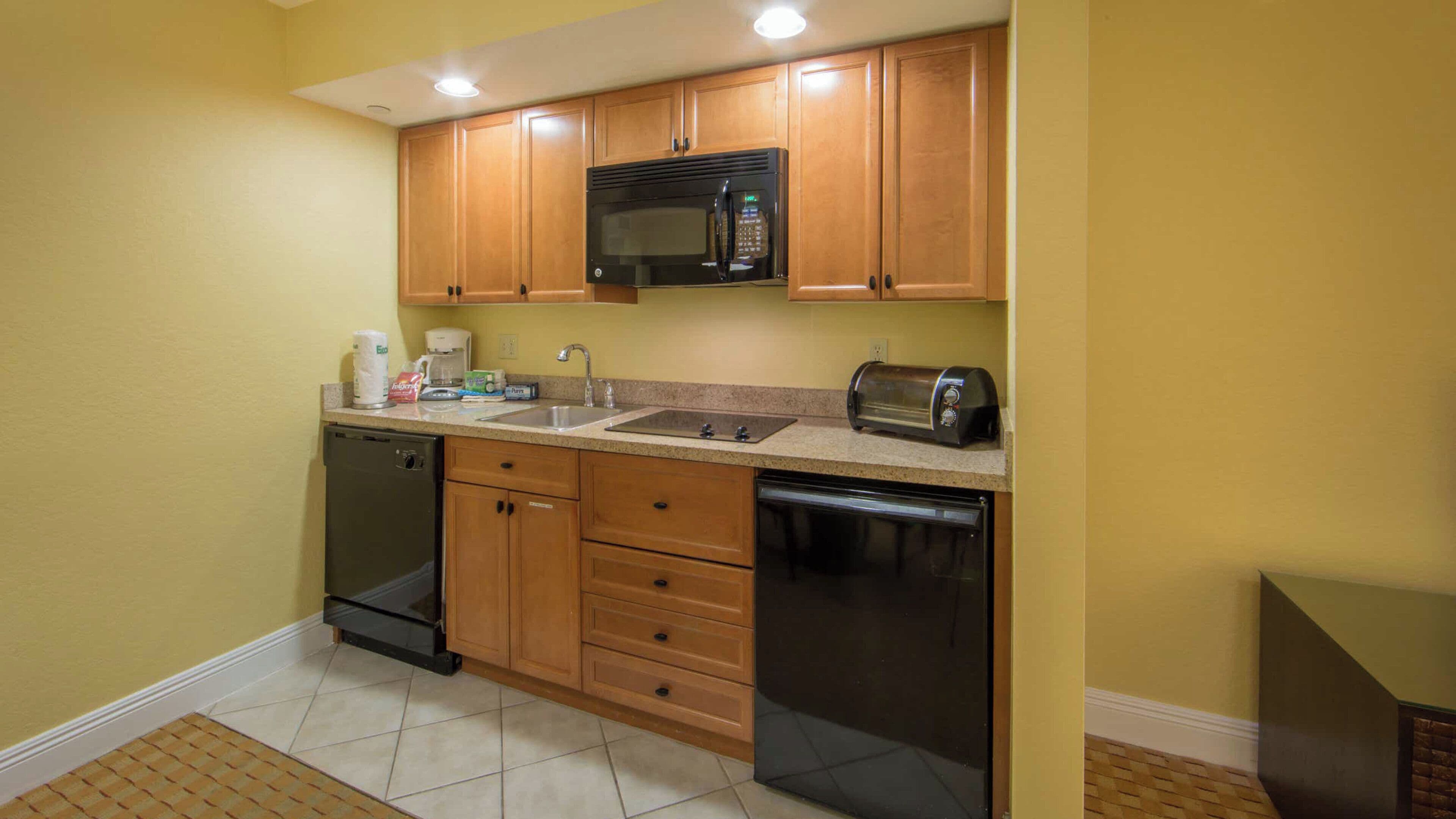 A compact kitchen with wooden cabinets, a built-in microwave, a toaster, and a dishwasher.