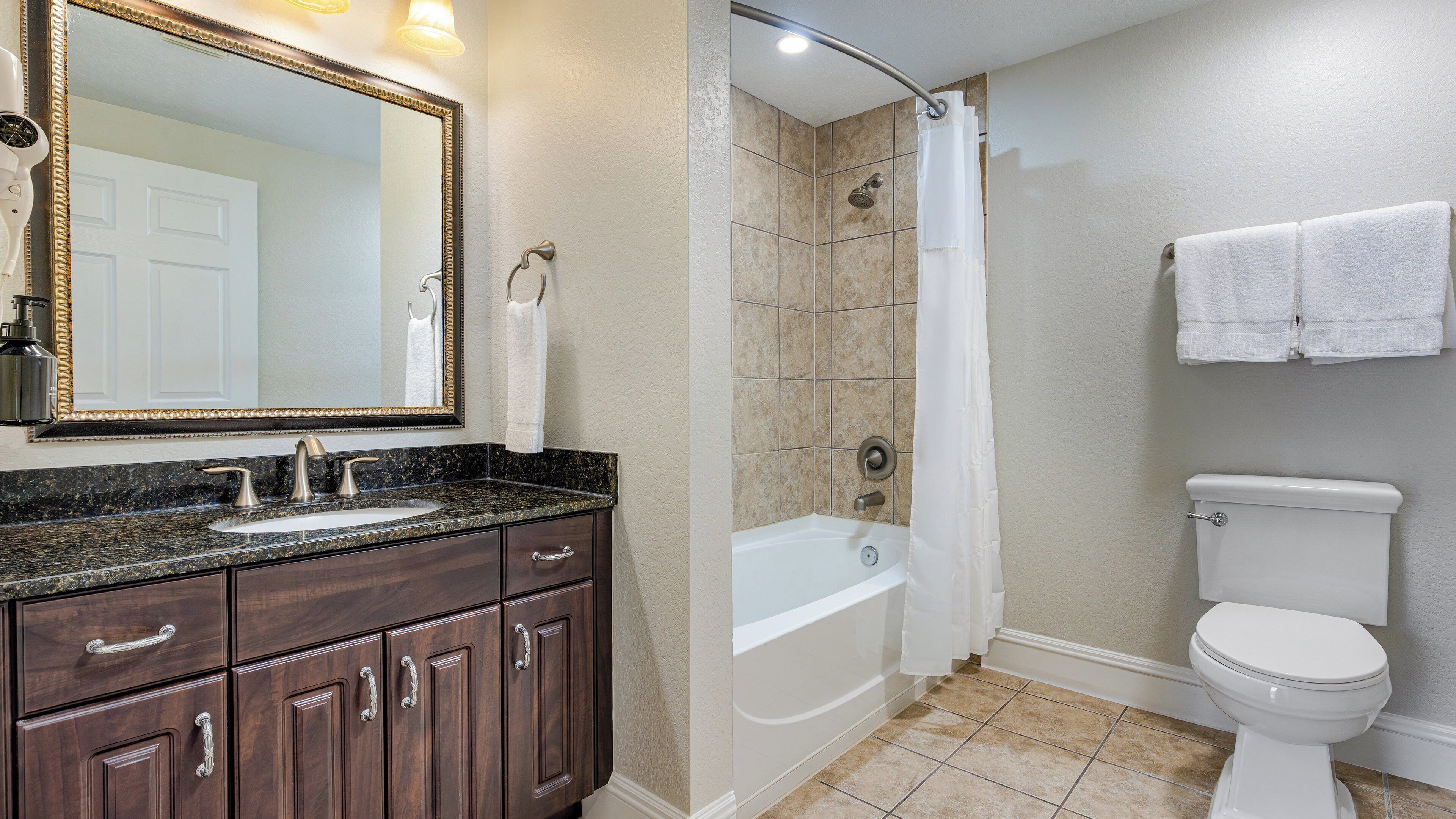 A bathroom with a sink, vanity, mirror, shower, and toilet.