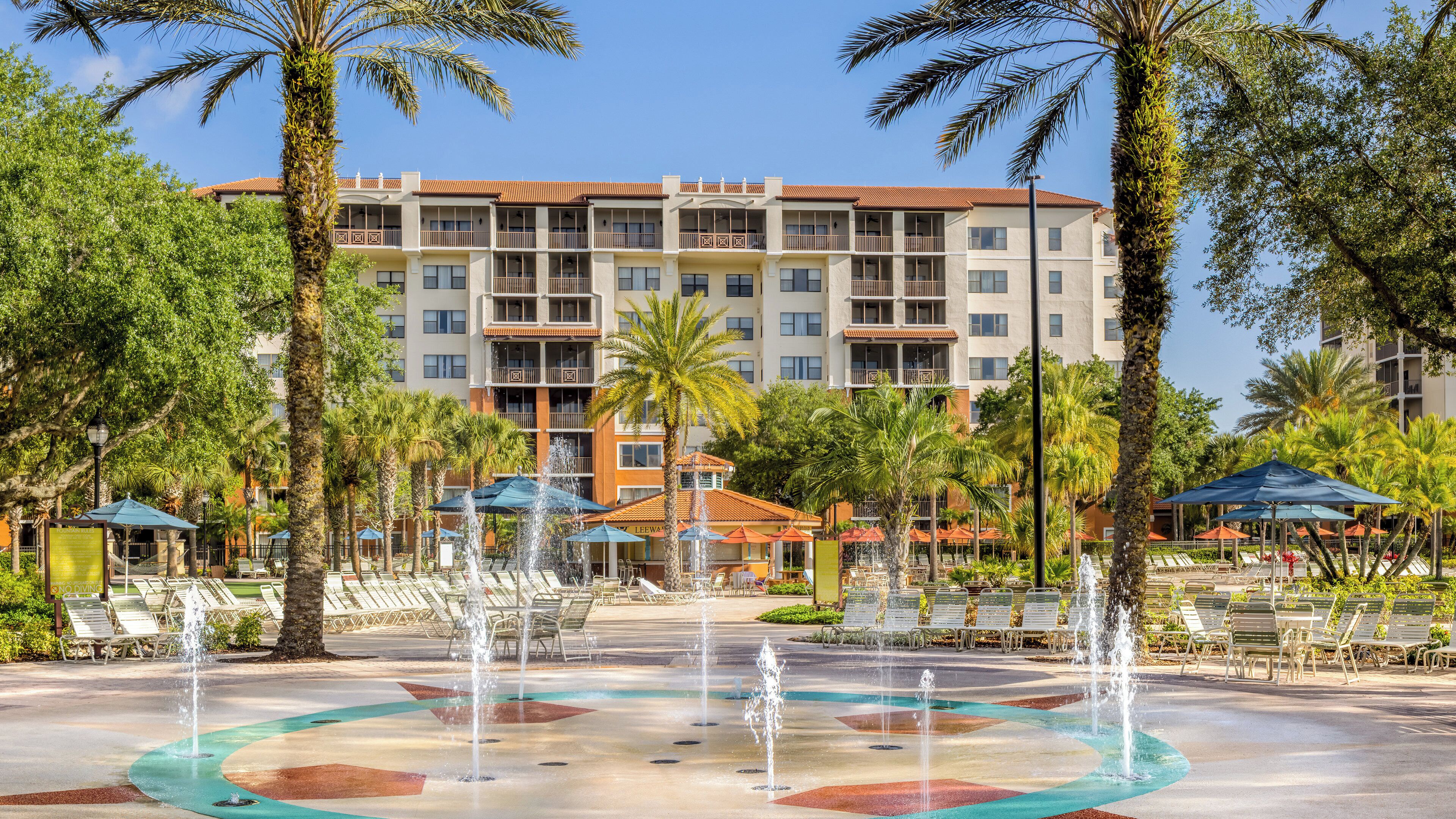 Un hotel con zona de piscina que incluye fuentes, sillones de descanso y sombrillas.