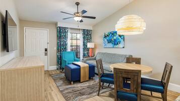 A modern living room with a ceiling fan, a dining table with chairs, a sofa, and a TV mounted on the wall.