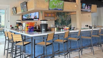 A bar area with multiple seating options, a counter with various beverages, and screens displaying sports events.