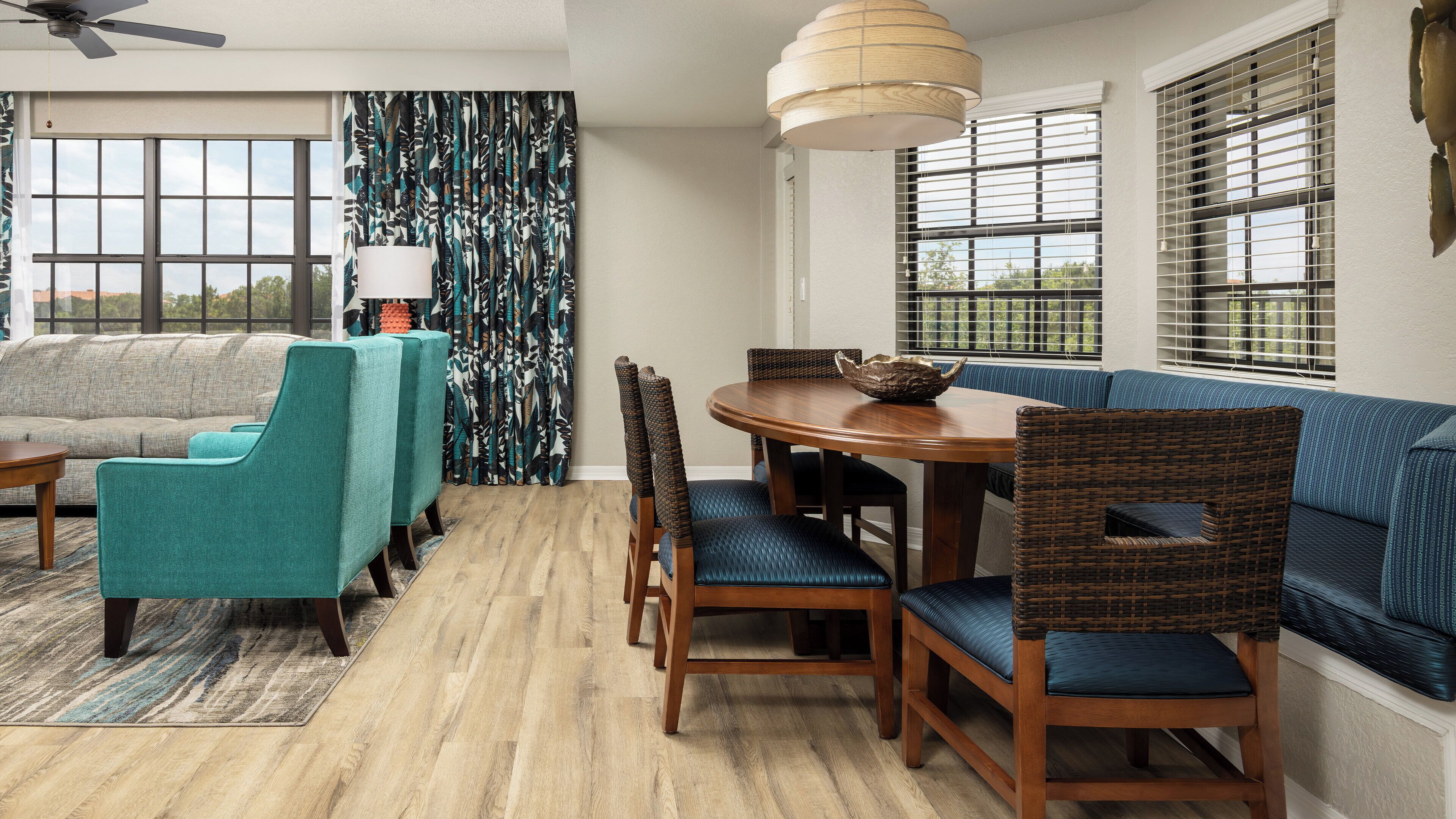 A dining area with a round wooden table, blue upholstered chairs, and a woven bench.