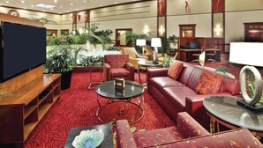 A spacious lobby with a red carpet, leather seating, a flat-screen TV, and various plants. - Columbus Airport Marriott (Columbus)
