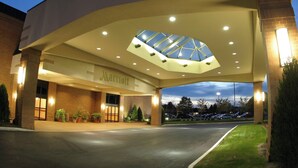 A Marriott hotel entrance with a covered walkway, potted plants, and a parking lot visible in the background. - Columbus Airport Marriott (Columbus)