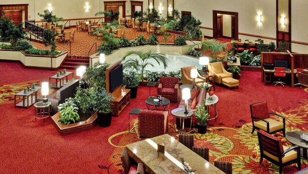 A spacious lobby with multiple seating areas, a central water feature, and numerous potted plants. - Columbus Airport Marriott (Columbus)