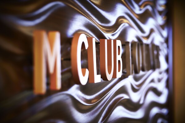 Primer plano de una pared metálica con la inscripción 'M CLUB' grabada.