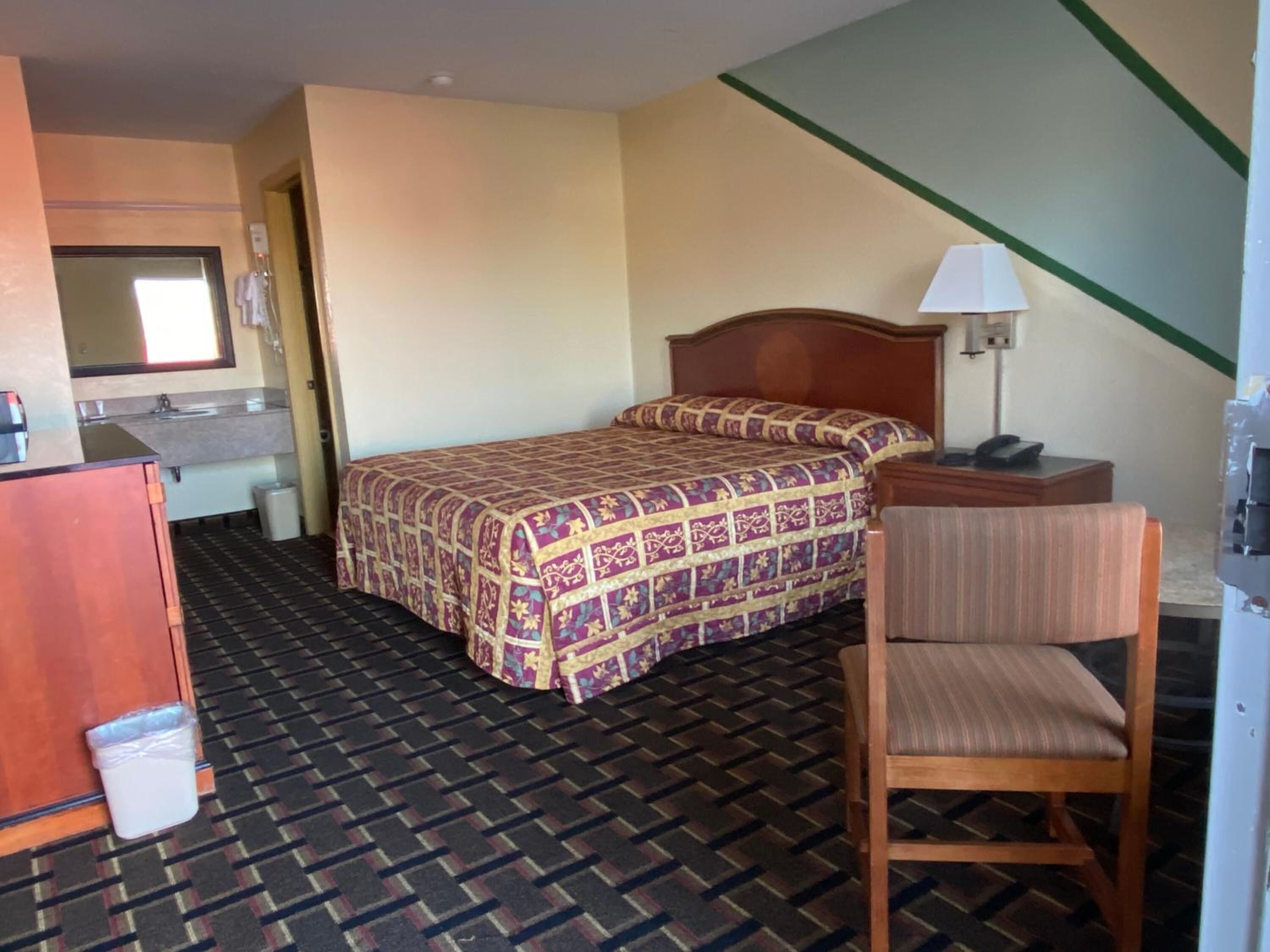 A hotel room with a bed, a desk, a chair, a mirror, and a bathroom.