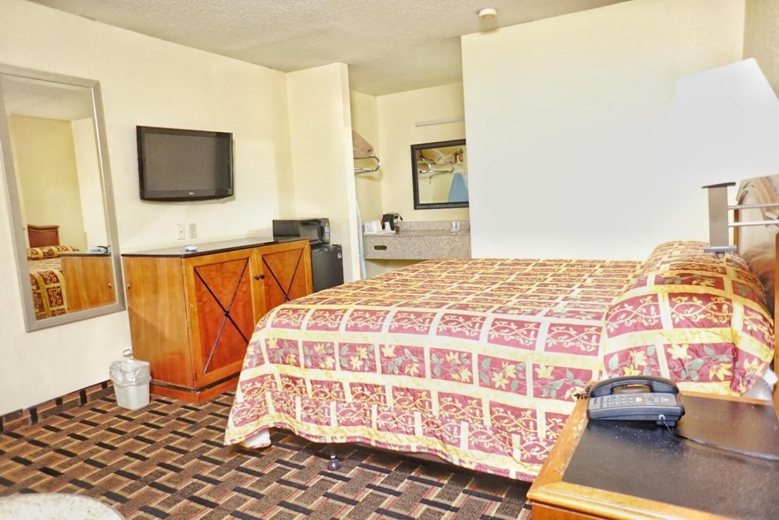 Une chambre d’hôtel comprenant un lit, un bureau avec un téléphone, une armoire, une télévision et une salle de bain avec un miroir et un lavabo.