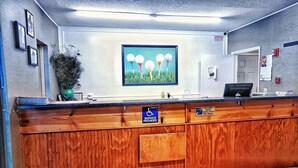A reception desk with a check-in sign, a framed artwork of golf balls, and a plant.