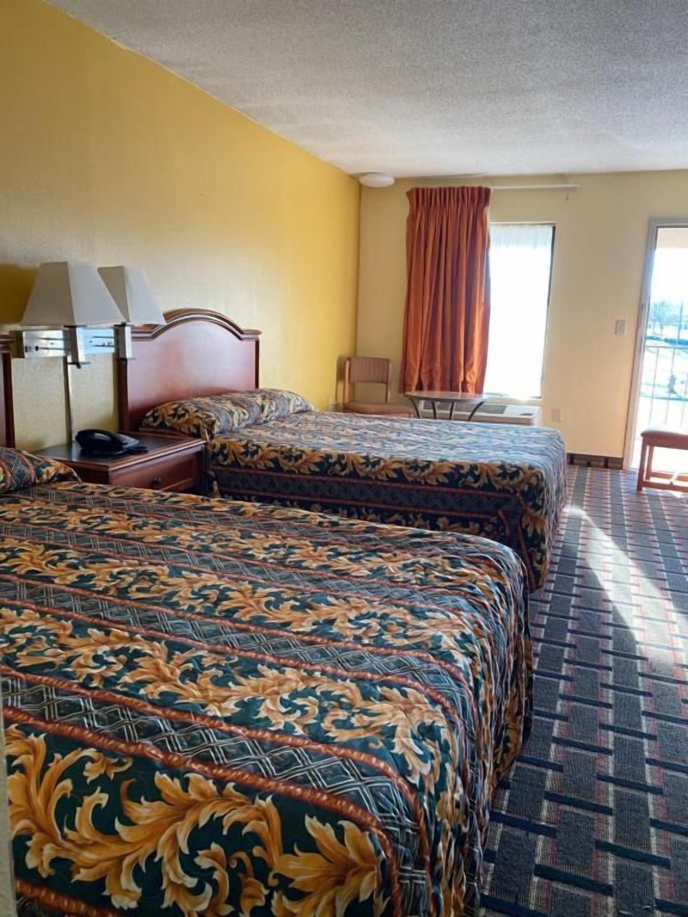 A hotel room with two beds, a desk, a chair, and a window with curtains.