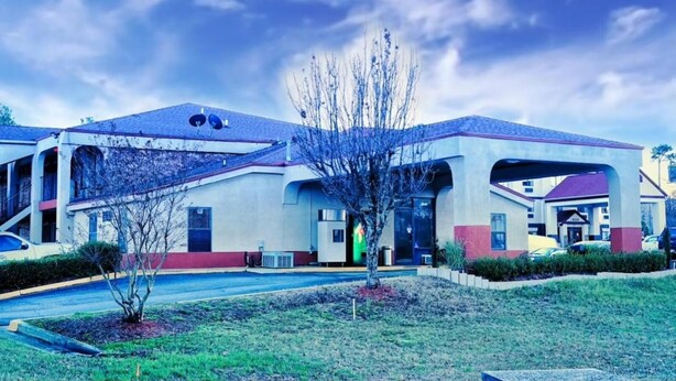 A motel with a central parking area, a covered outdoor seating area, and a small garden with a tree.