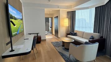 Habitación de hotel moderna con una televisión de pantalla plana, un sofá, una mesa de centro y un escritorio con una silla.