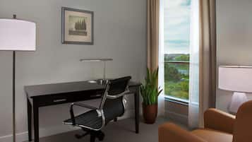 Habitación de hotel con escritorio, silla de oficina, planta en maceta y vistas al exterior.