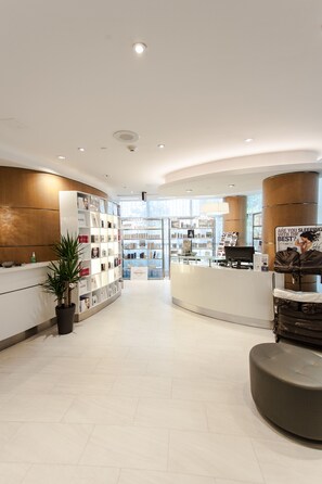 A modern hotel lobby with a reception desk, a seating area, and a display of products.