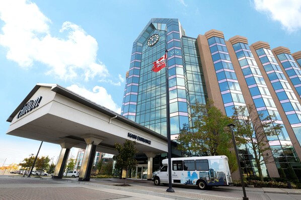 A hotel with a modern glass facade, a prominent clock, and a 'Main Entrance' sign.