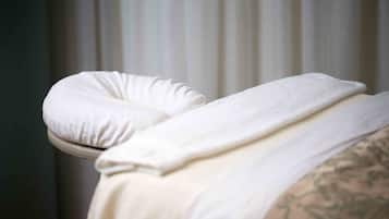Una cama con un almohadón y una manta blancos.