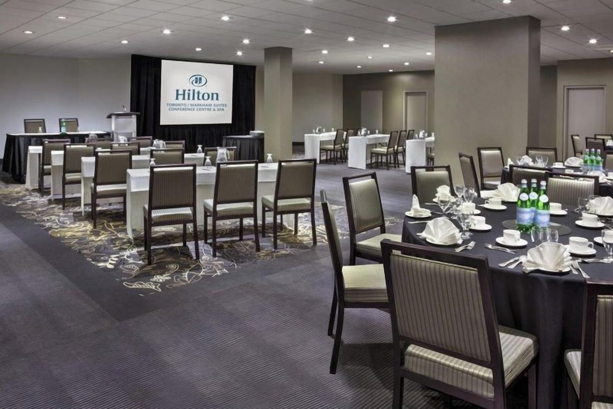 A conference room with multiple tables, chairs, and a presentation screen at Hilton Toronto Markham Suites.