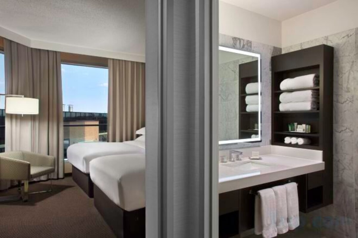 Ein Hotelzimmer mit einem großen Bett, einer Sitzecke, einem Badezimmer mit Spiegel und Blick auf die Stadt.