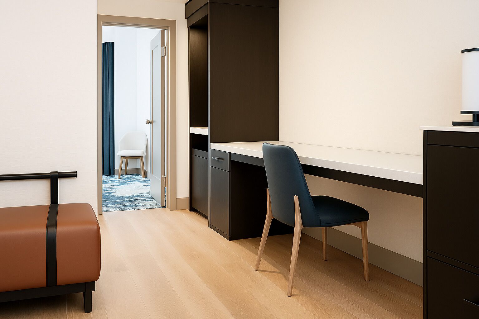 A modern hotel room with a wooden floor, a desk with a chair, a wardrobe, and a small seating area with a bench.
