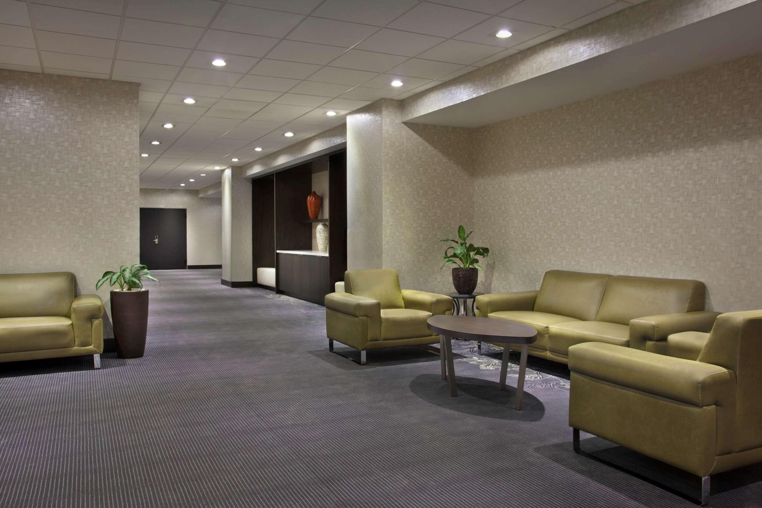 A spacious lobby with a carpeted floor, two sofas, a coffee table, and potted plants.
