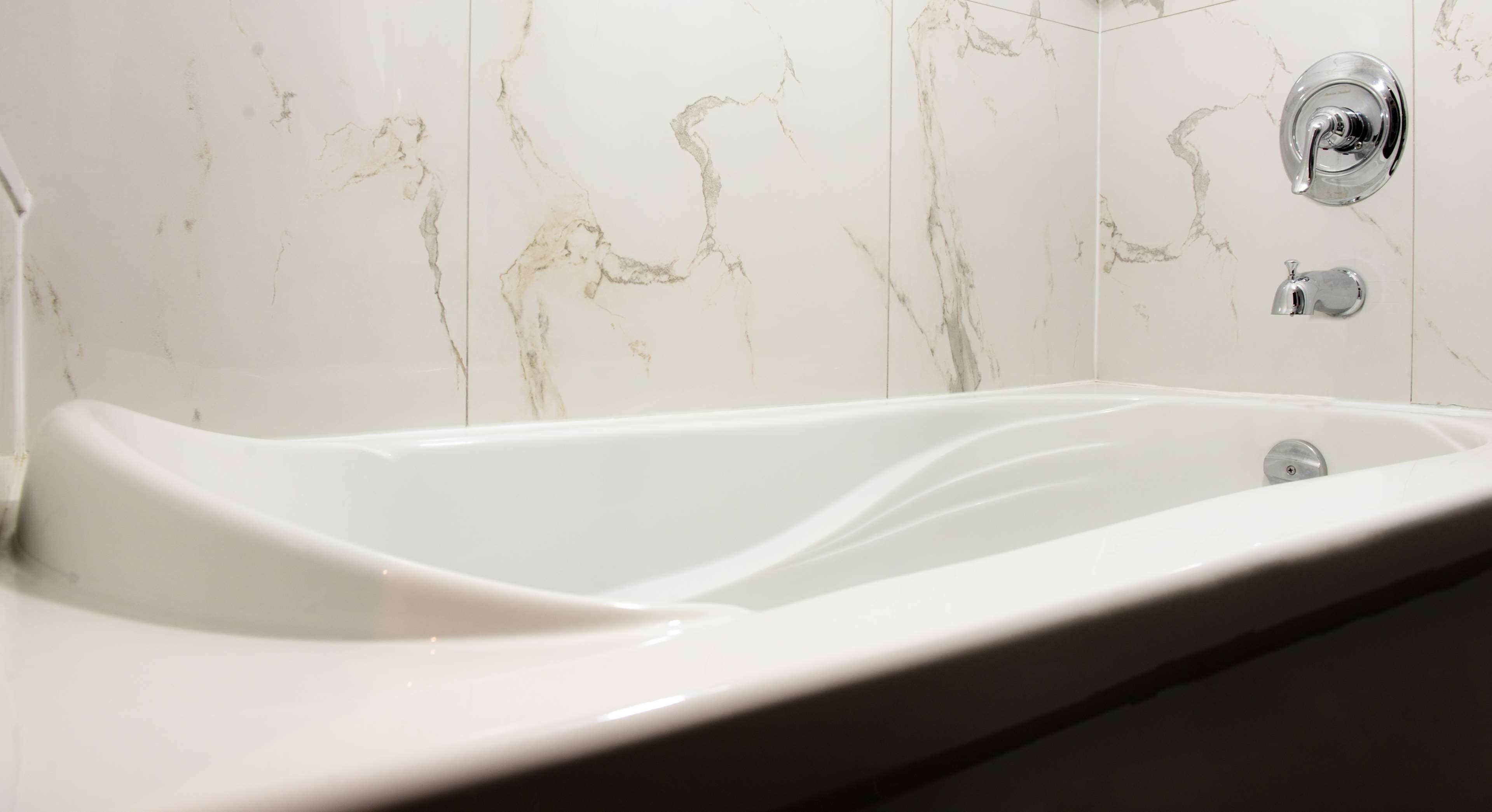 Un baño moderno con pared de mármol y bañera blanca.