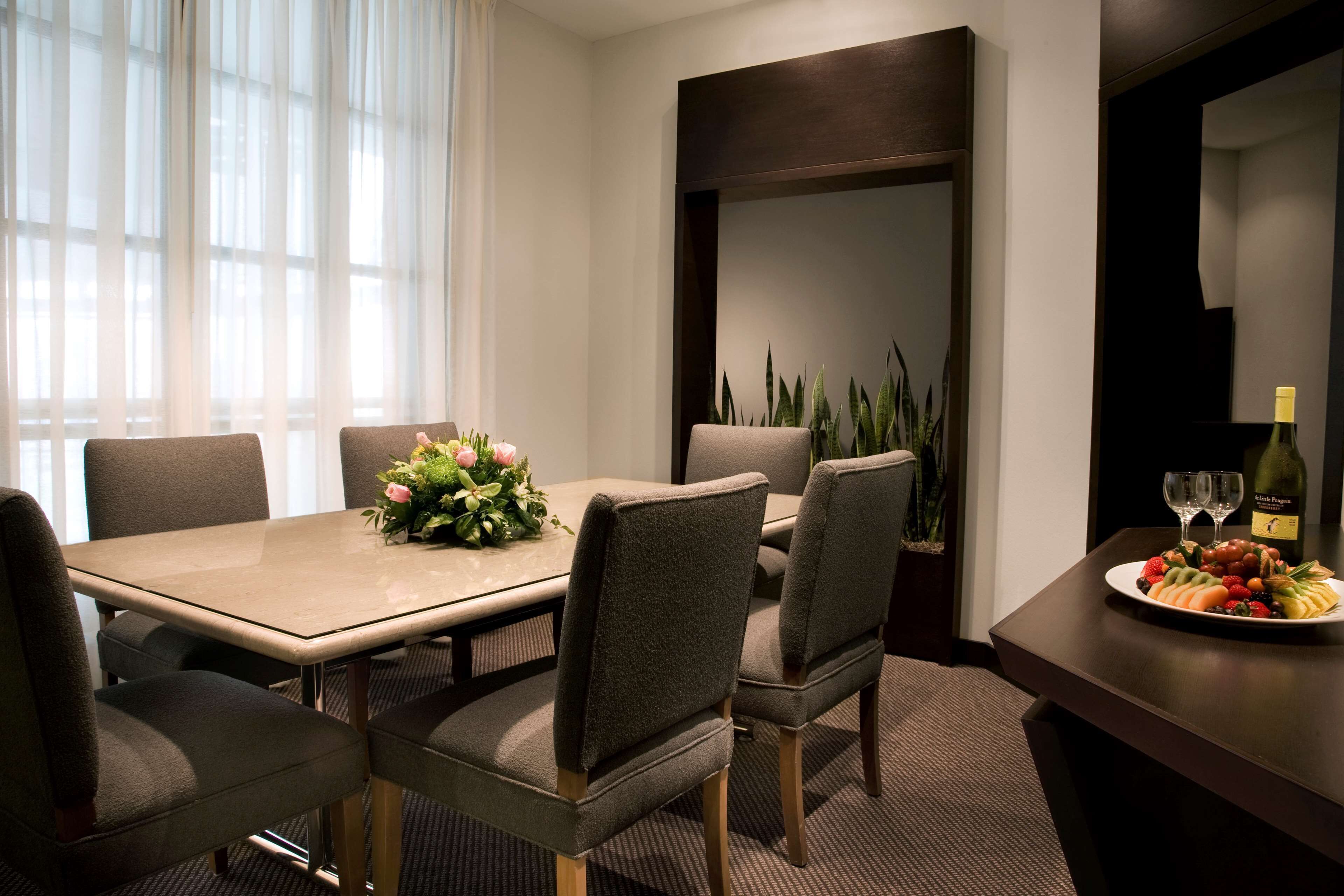 Un coin repas avec une table dressée pour six personnes, un centre de table composé de fleurs et une assiette de fruits à proximité.