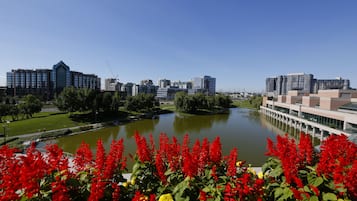 Un ensemble immobilier moderne composé de plusieurs bâtiments, avec un grand plan d’eau à l’avant, entouré de verdure et de fleurs rouges.