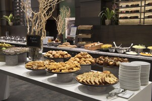 Un bufé con diversos pasteles y panes, incluyendo croissants y barras, dispuesto en una barra con platos y utensilios de servicio.