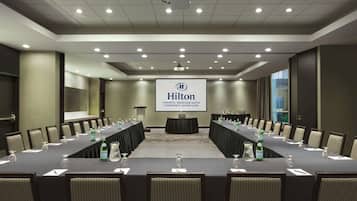 Un salón de conferencias con una larga mesa, sillas y una pantalla que muestra el logotipo de Hilton.