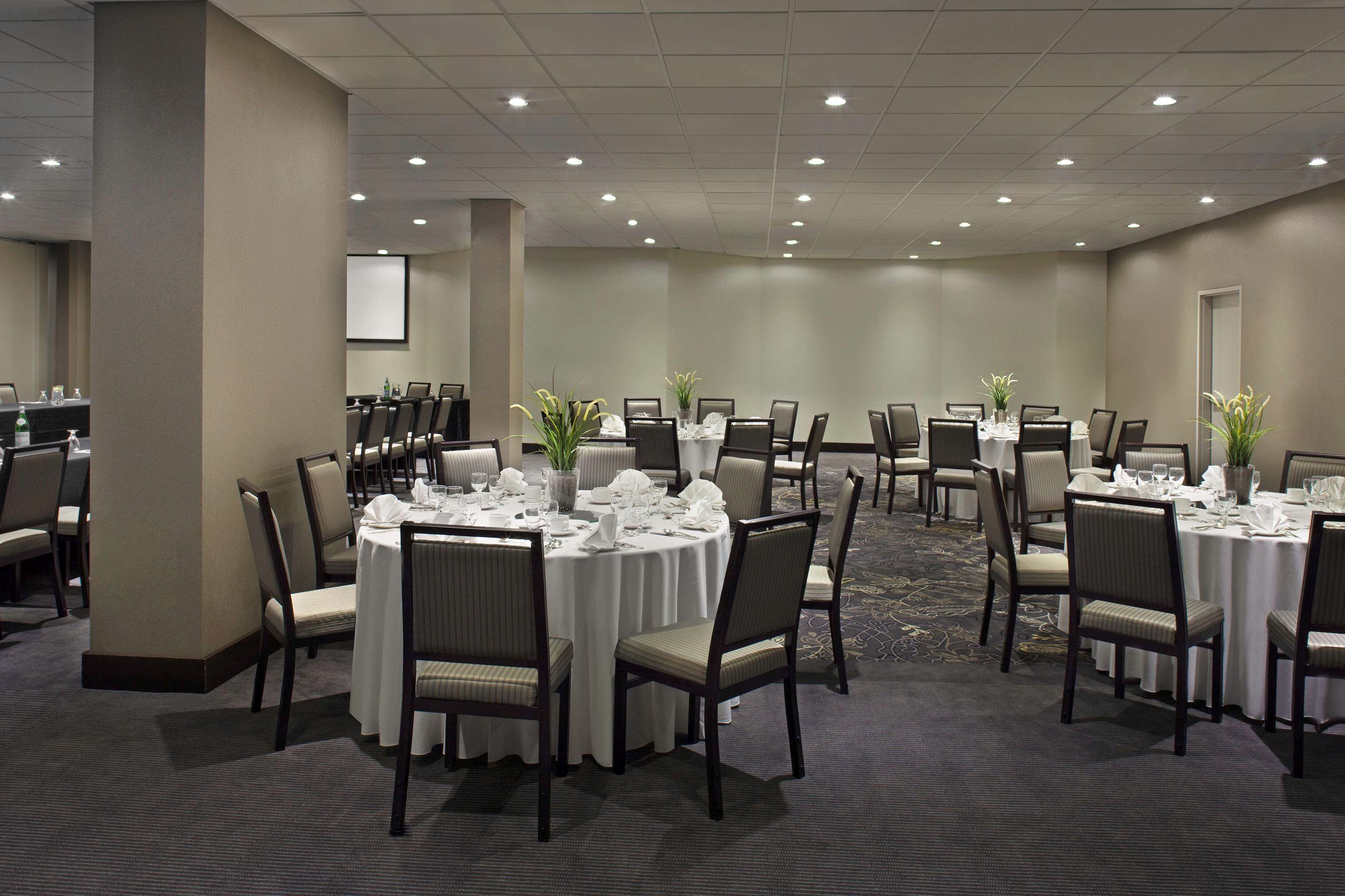 A conference room with round tables, chairs, and a projector screen.