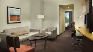 A hotel room with a sofa, armchairs, a desk, and a flat-screen TV.