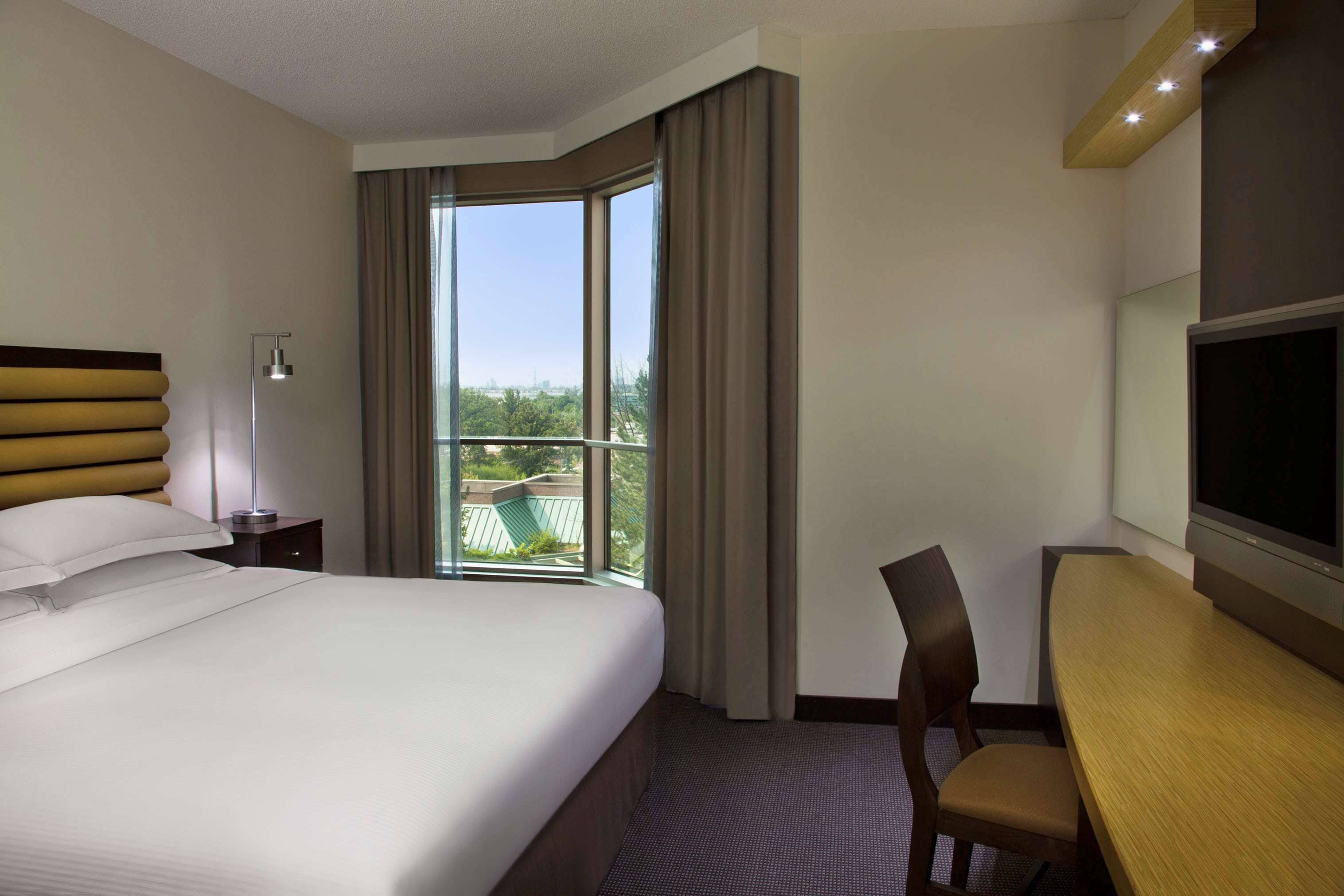 Een hotelkamer met een groot bed, een bureau, een stoel, een televisie en een raam met gordijnen.