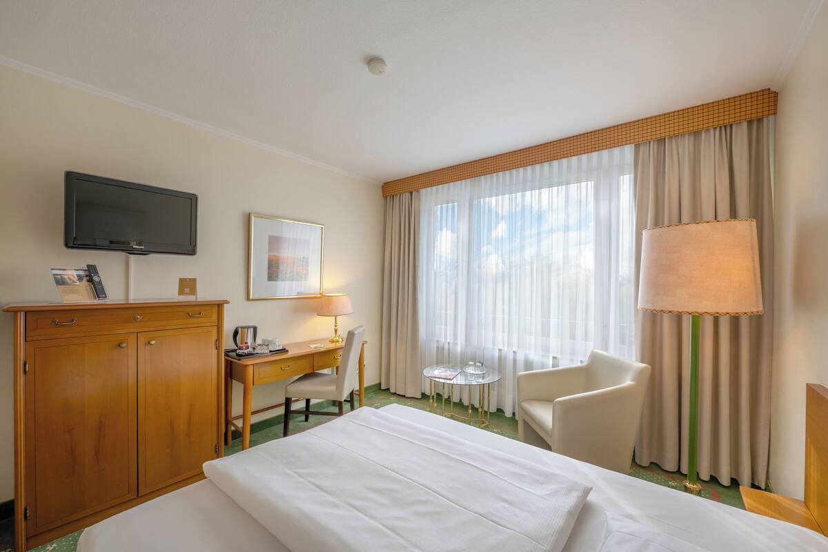 Ein Hotelzimmer mit Bett, Schreibtisch, Stuhl, Fernseher und einem fenster mit Vorhängen.